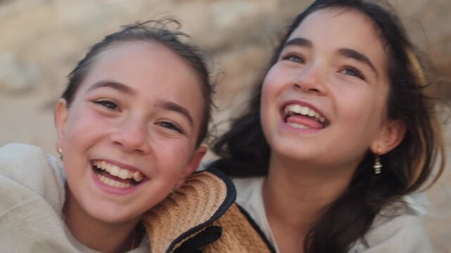 Cheerful young sisters wrapped in blanket laughing together at beach showing happiness, bonding and connection