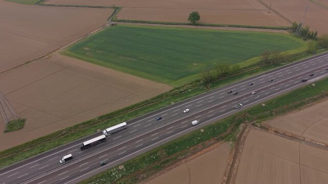 Aerial Highway View: A high-angle drone shot captures a modern highway stretching through vast agricultural fields, with trucks and cars navigating the lanes.