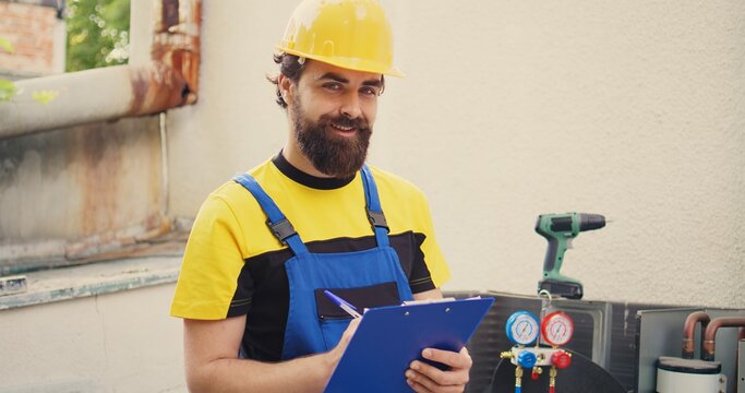 Expert technician doing inspection of freon levels and necessary repairs to prevent major breakdowns. Seasoned mechanic troubleshooting hvac system, writing findings on clipboard