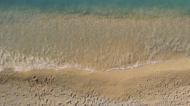 Aerial top down view of sea waves gently wash onto sandy beach in Greece