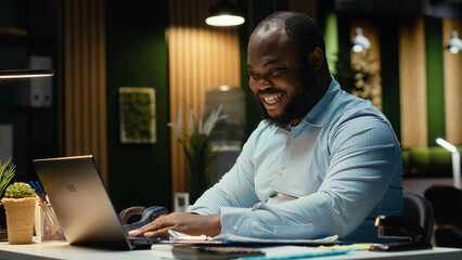 Fototapeta premium Excited african american man receiving good news for career opportunity, being proud of his breakthrough and accomplishment in the office late at night. Delighted about new deal.