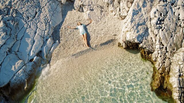 Relaxed woman lies peacefully on a stony beach enclosed by rugged white cliffs