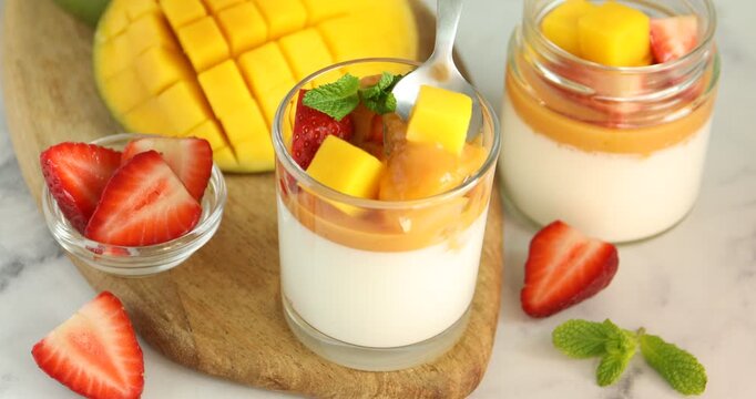 Woman eating delicious mango panna cotta at white marble table, closeup