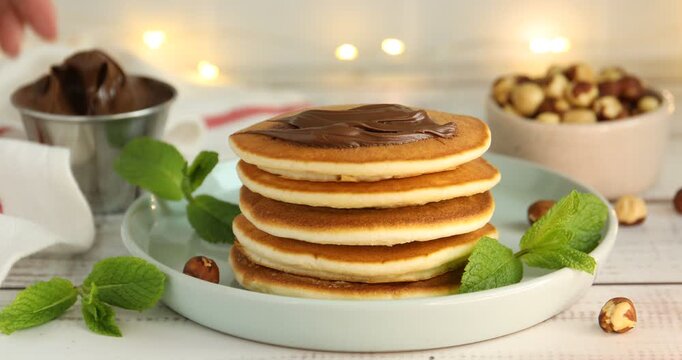 Woman spreading chocolate paste onto pancake at light wooden table, closeup