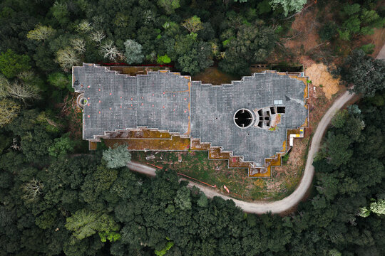 Aerial view of the unique architecture of Sammezzano Castle with its flat roof and circular courtyard surrounded by dense green forest and a winding road in Leccio, Toscana, Italy.