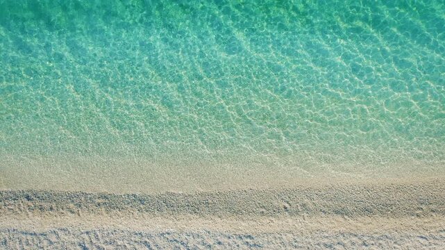 Top down view of soft white sand beach meeting transparent turquoise waters in Greece