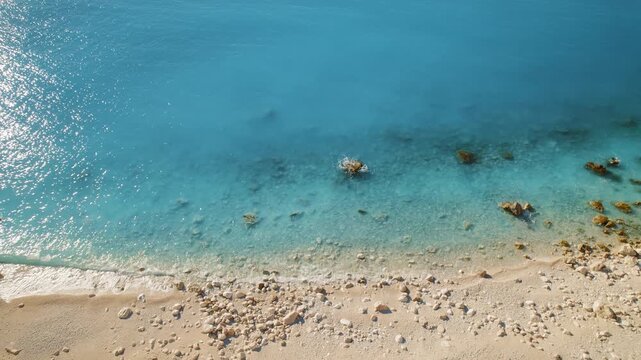 Gentle waves lap a quiet rocky beach where turquoise sea waters meet tan pebbles