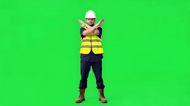 Construction worker in hard hat and reflective vest making a stop gesture with crossed arms on green screen background