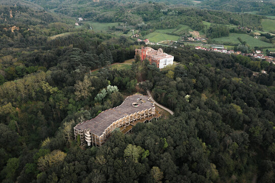 Aerial view of the abandoned hotel structure and the historic Castello di Sammezzano nestled within a dense green forest on the rolling hills of Leccio, Toscana, Italy.