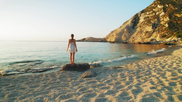 Woman standing on rocky shore at sunset on Petani Beach, Kefalonia Island Greece