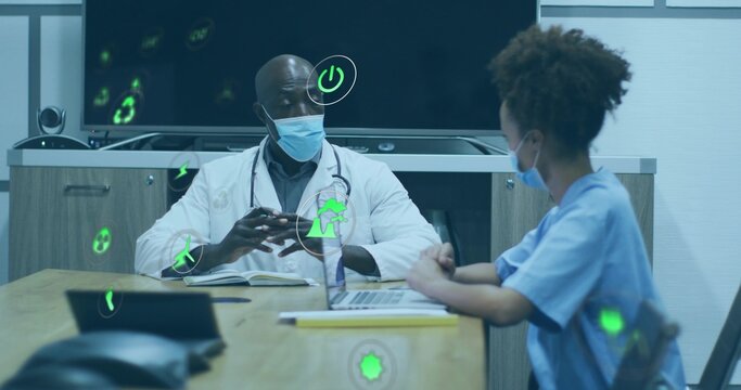 Consulting doctor in white coat, steth, masked scrub nurse reviewing display laptop at clinic table