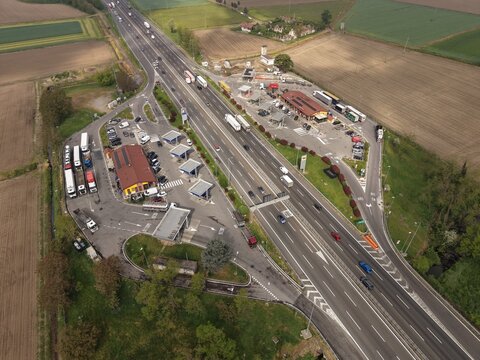 Aerial View of Highway a 50 Rest Stop: An expansive drone shot captures a busy highway rest stop with multiple vehicles, including trucks and cars, dispersed among service buildings, fuel stations.