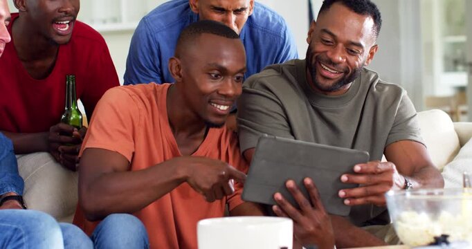 Diverse men on couch, orange shirt pointing at tablet, everyone leaning in to view and laugh