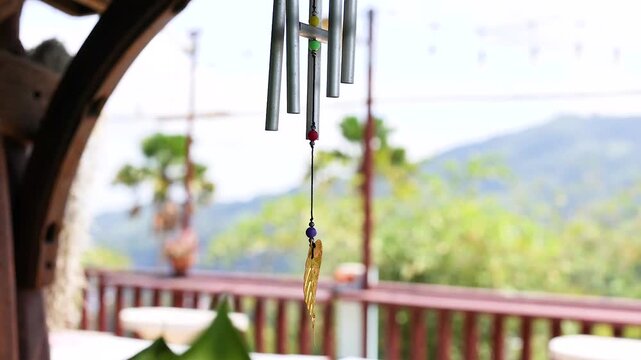Metal wind chime with golden leaf pendant swinging in breeze on tropical mountain balcony.