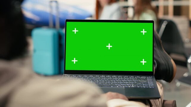 Green screen laptop with African American travelers in crowded airport waiting area before flight departure. Luggage and boarding procedures in the background, nomadic lifestyle.