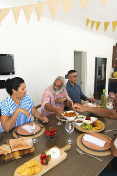 Diverse family passing dishes and talking at home dining table with pasta and wine