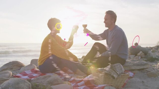 Mature couple clinking glasses on checkered blanket at sunset, initiating animated glitches for ads