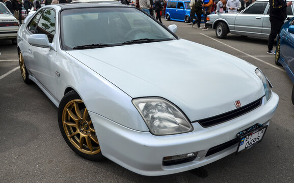 White Honda Prelude with gold multi-spoke wheels. This fifth-generation coupe is a JDM classic, known for its sleek profile and cultural impact in the 1990s