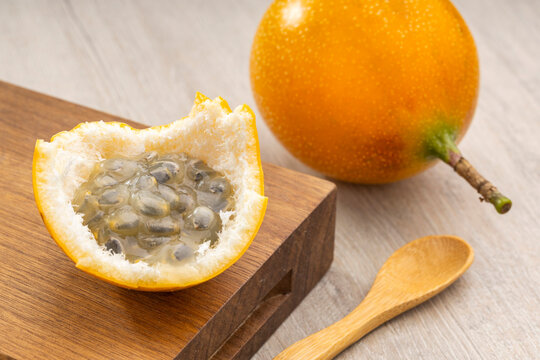 Tropical granadilla fruit (Passiflora ligularis) with visible seeds, food still life with a wooden spoon and light background.