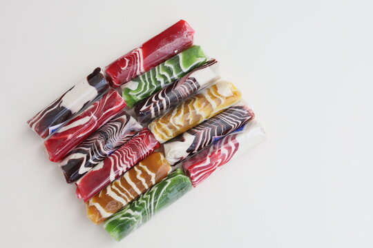 A dozen of Dodol Garut, traditional Indonesian sweet taffy, with colorful striped patterns in red, green, and brown, isolated on a white background.