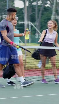 Vertical video: Four tennis players walking court crossing net, handing yellow bottle and chatting