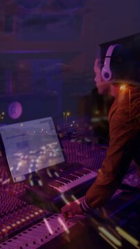 Vertical video: DJ tweaking faders and playing keys after laptop cue to mix under city overlay