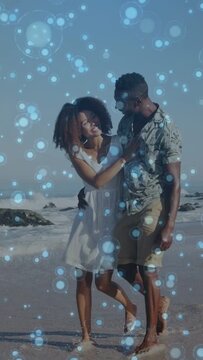 Vertical video: Waves nudging couple walking sand leaning sharing love hand on chest bokeh drifting