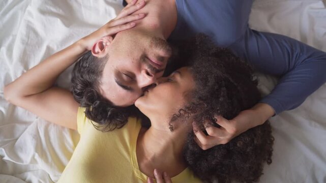 Latino young couple lying down together on bed in cozy bedroom at home.