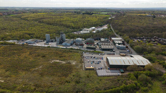 Aerial view of the Tarmac construction materials site with industrial buildings, silos, and a parking lot surrounded by lush woodland in Swadlincote, England, United Kingdom.