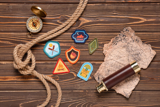 Scout badges with rope, map, spyglass and compass on wooden background