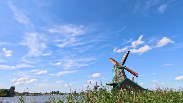 Cinematic shot of traditional dutch windmill spinning under blue sky with fluffy white clouds in Zaanse Schans.