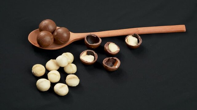 Whole and cracked macadamia nuts with wooden spoon on dark background.