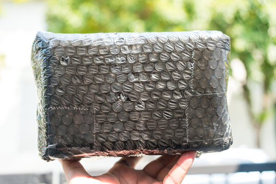 Parcel wrapped in dark black metallic bubble for secure shipping or storage on hand