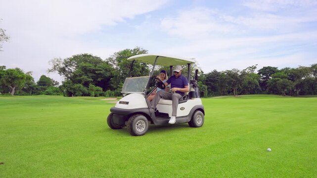 Asian golfer team ride in golf cart together on a scenic golf course. 