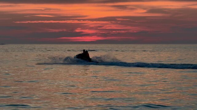A young couple riding a jet ski on the Andaman Sea during a beautiful sunset at Patong beach in Phuket. Romantic water sport activity, summer vacation travel and extreme adventure in Thailand.