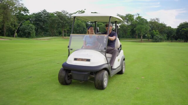 Asian golfer team ride in golf cart together on a scenic golf course. 
