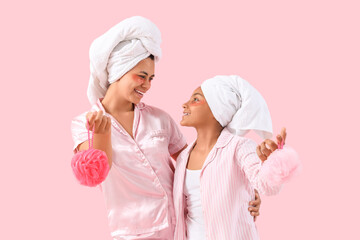 Happy young African-American mother and her daughter in pajamas with under-eye patches holding bath...
