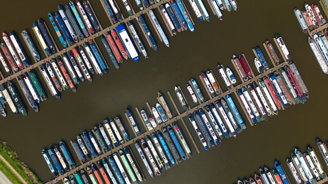 Aerial view of colorful narrowboats moored at Barton Marina with wooden piers and dark water in Barton-under-Needwood, England, United Kingdom.