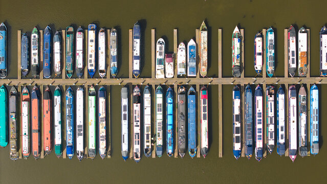 Aerial view of Barton Marina with colorful narrowboats moored at wooden jetties on calm water in Barton-under-Needwood, England, United Kingdom.