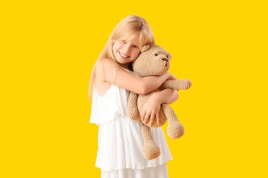 Cute little girl with plush teddy bear on yellow background