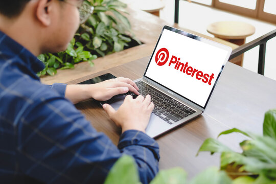 Bangkok, Thailand. April 17, 2026; An over the shoulder view of a man using a laptop displaying the Pinterest social media logo while sitting at a wooden table in an outdoor cafe.