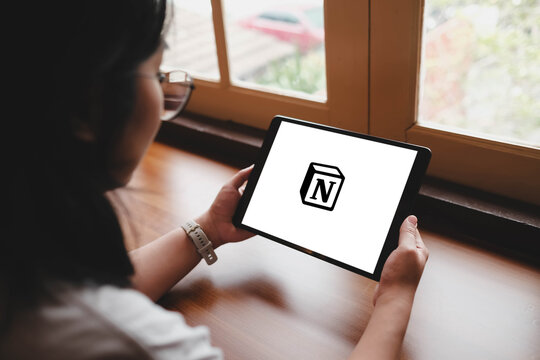 Bangkok, Thailand. April 16, 2026; A woman holds a tablet displaying the Notion productivity software logo while sitting by a window with natural sunlight.