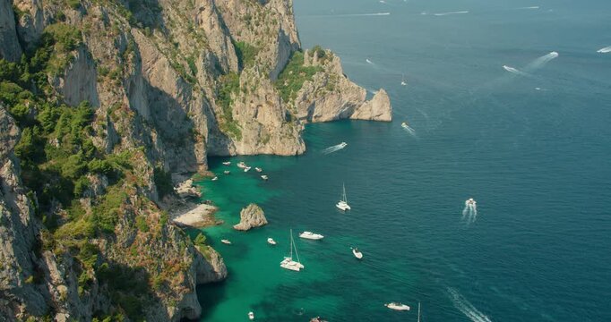 Steep rocky cliffs and turquoise coves filled with boats create a vivid summer scene in Capri Italy