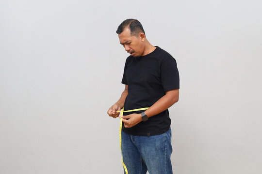 Standing side view of a man measuring his waist or measuring his stomach circumference with a measuring tape, disappointed expression, concept of failed diet or obesity.