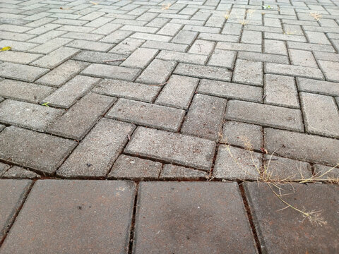 Close up of grey and brown interlocking brick pavement in herringbone pattern, outdoor walkway texture