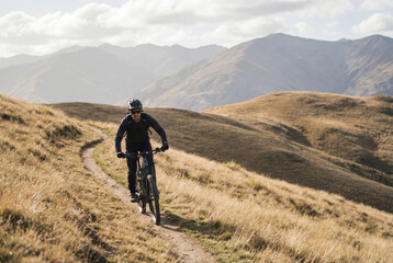 Fototapeta premium Male eMTB Rider Climbing Narrow Hillside Path Toward Distant Mountains