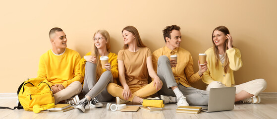 Group of students sitting on floor near pale yellow wall and drinking coffee