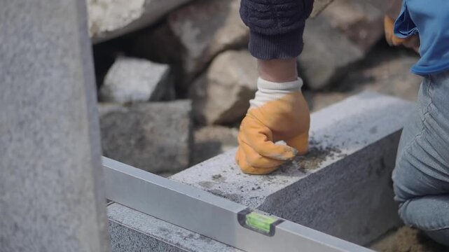 Worker uses hammer and level to build stone wall