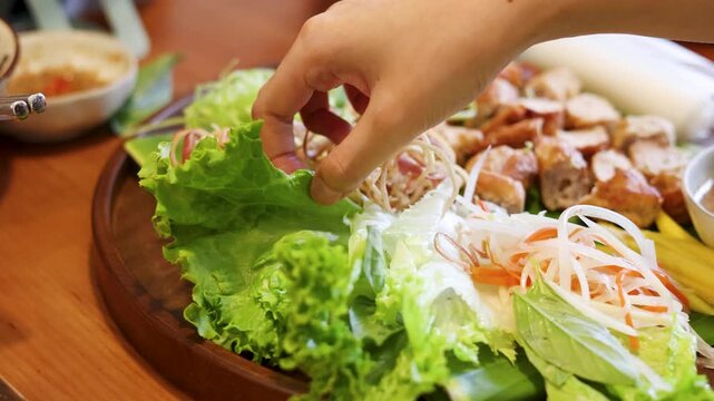 Hand Picking Fresh Lettuce from a Vietnamese Nem Nuong Platter