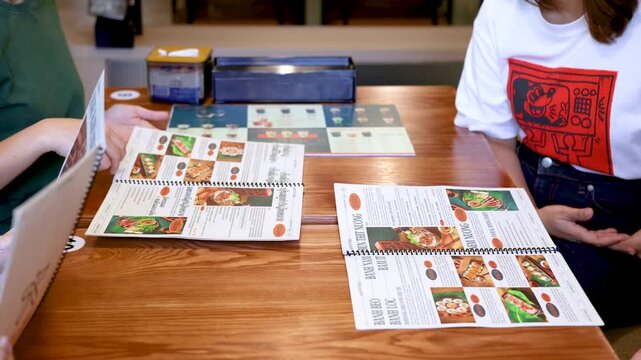 Asian Restaurant Customers Browsing Vietnamese Cuisine Menus on Wooden Table